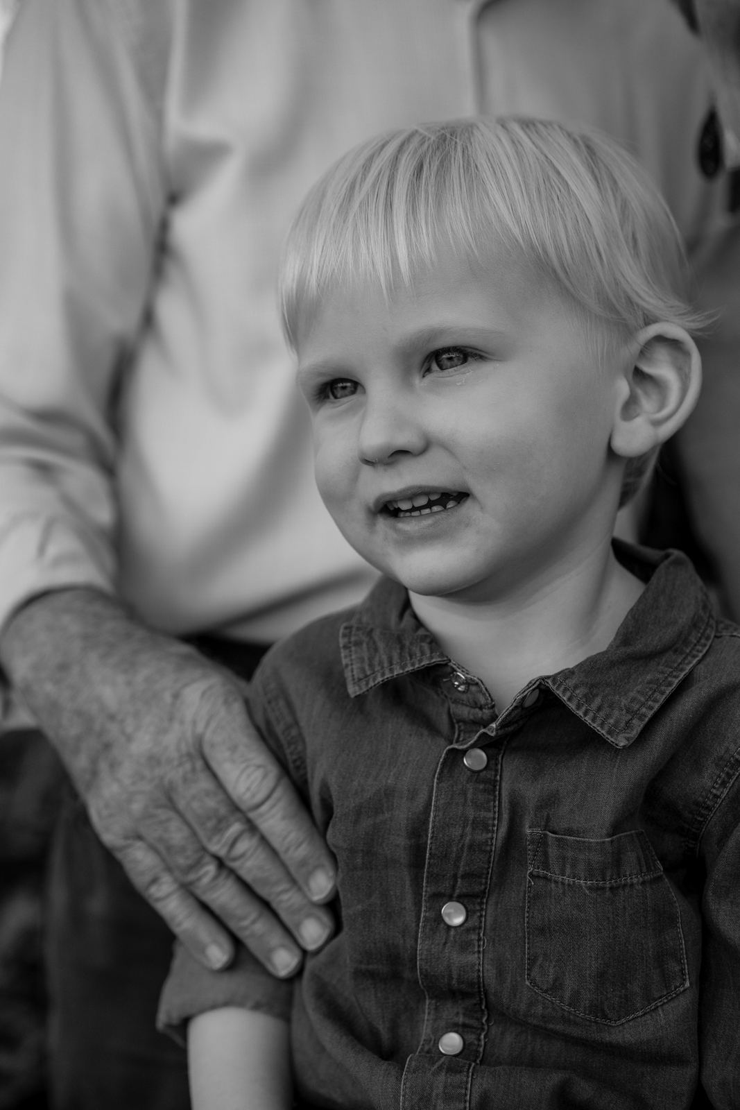 Black and white photo of a smiling little boy with a grandparent's hand resting on his shoulder