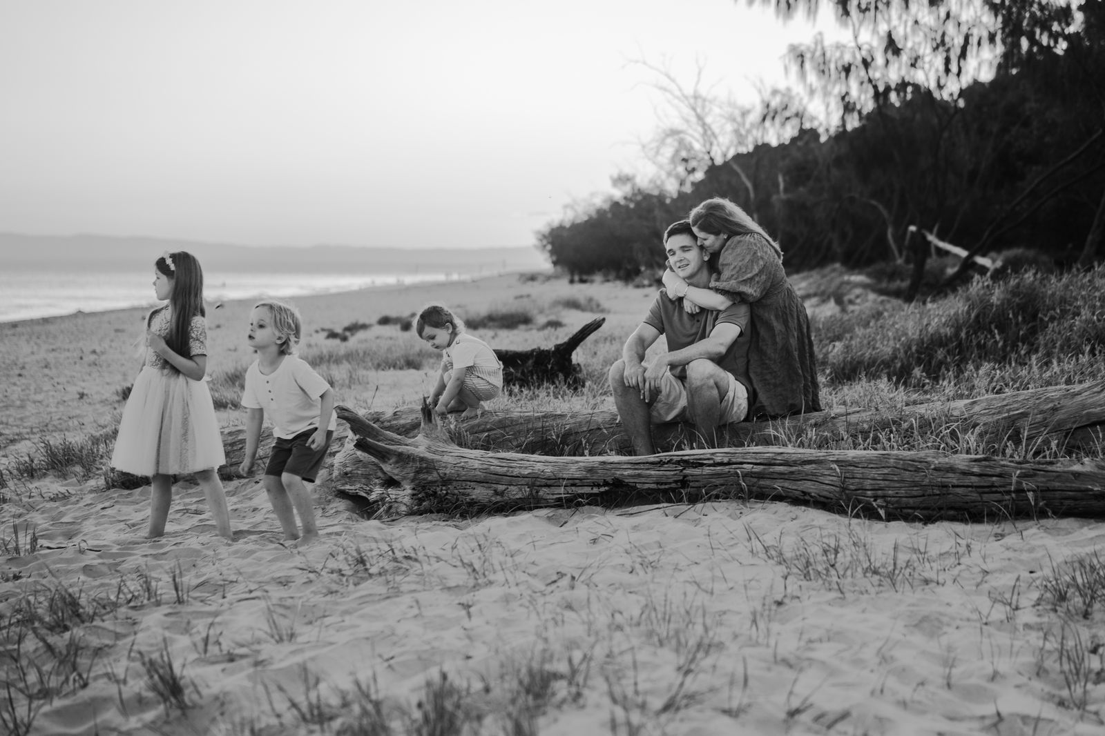 Black and white photo of a family sitting on a driftwood log by the beach
