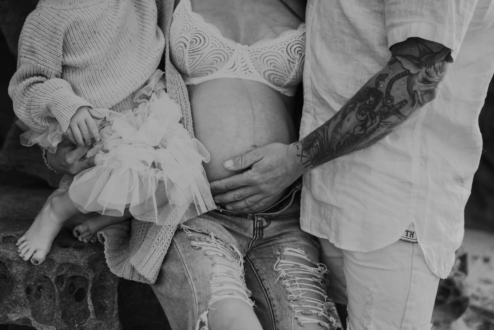 Black and white detail of family hands resting on a baby bump