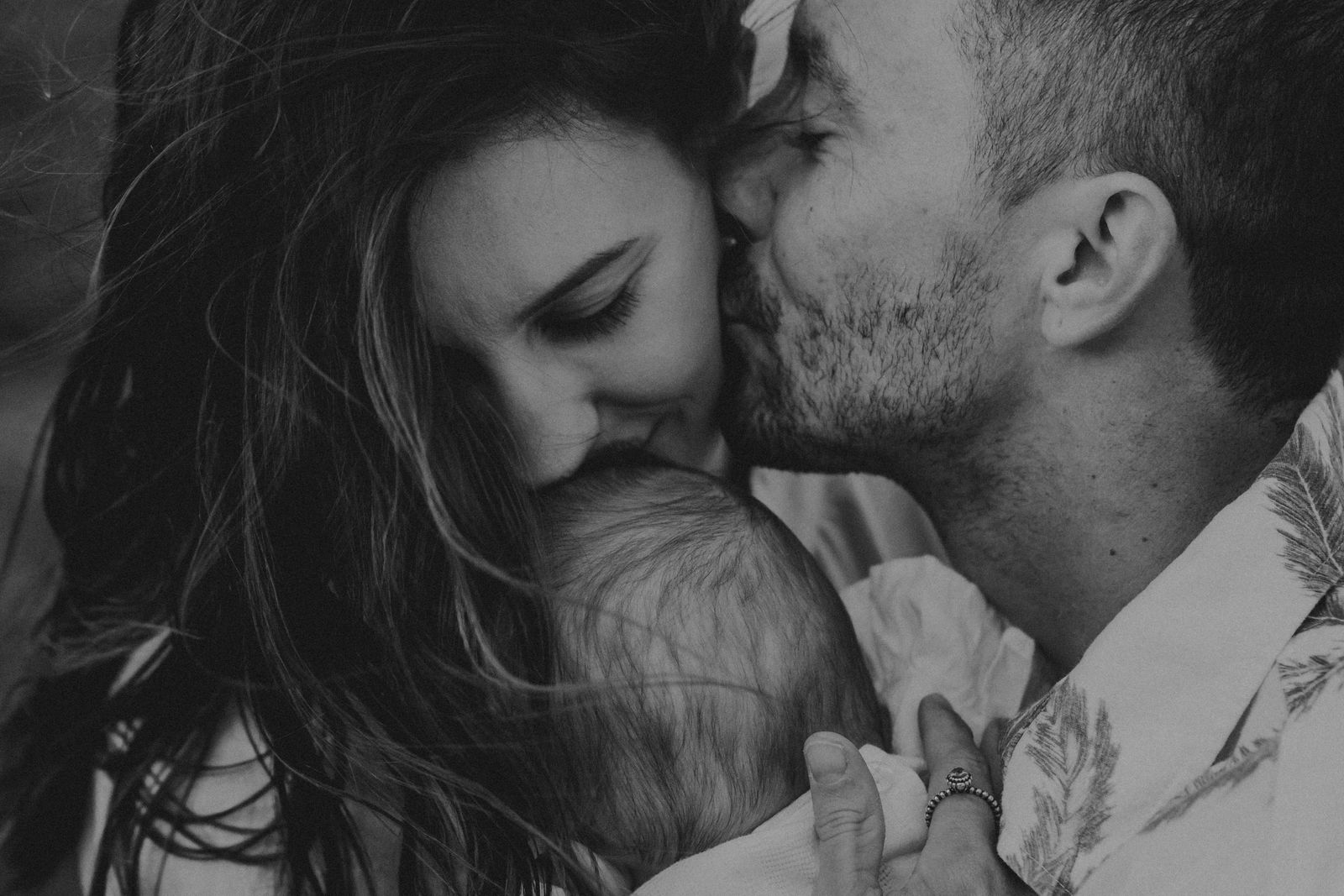 Black and white photo of parents kissing their newborn