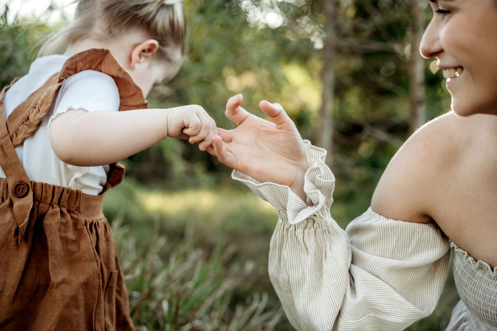 Little girl in a rust pinafore reaching for her mum's hand among the trees