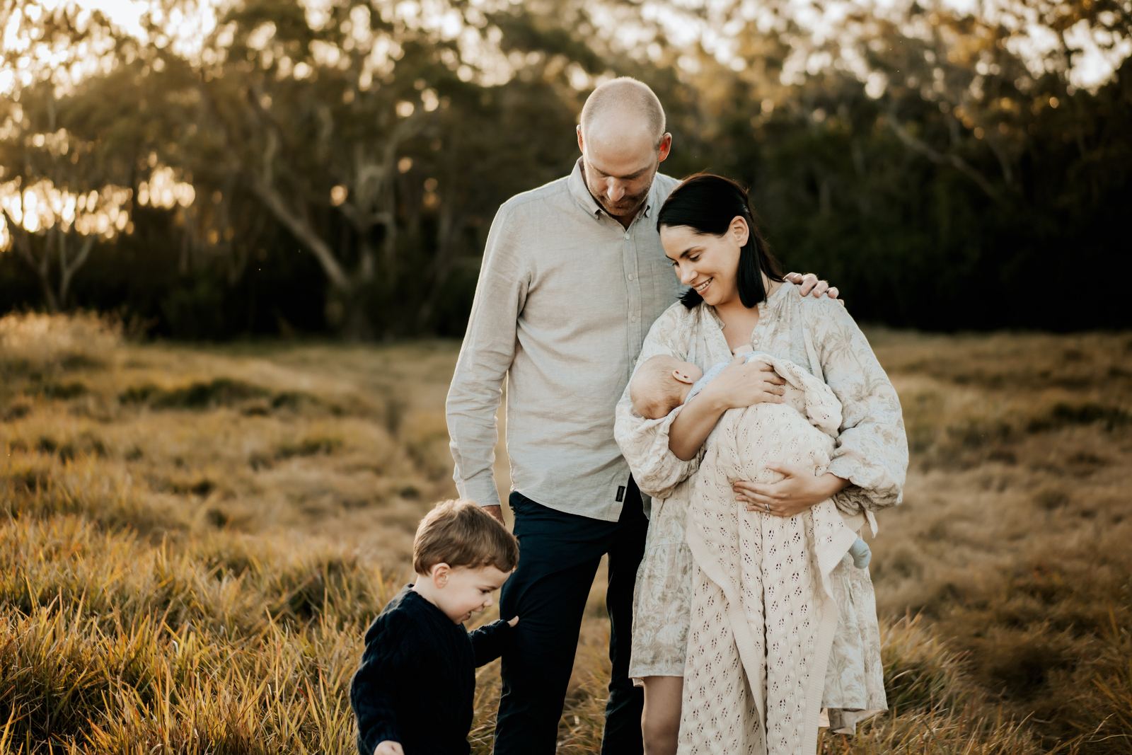 Expecting parents and their toddler in long grass at golden hour