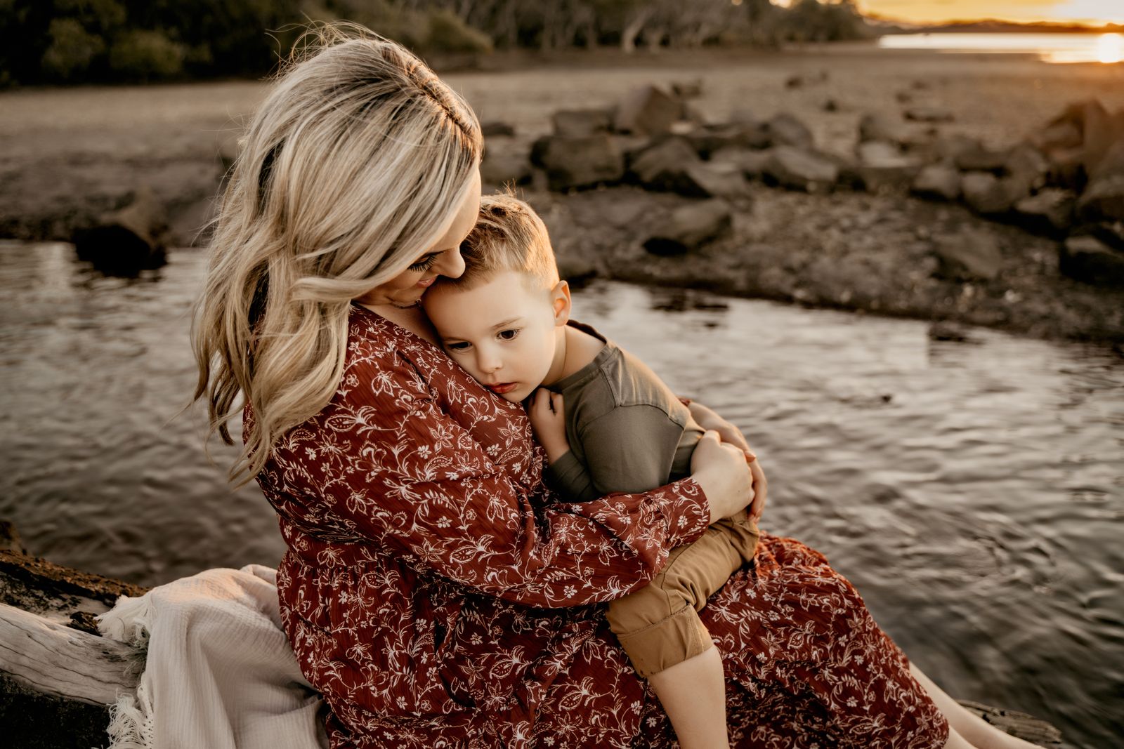 Mum in a floral dress cuddling her toddler beside a rock pool