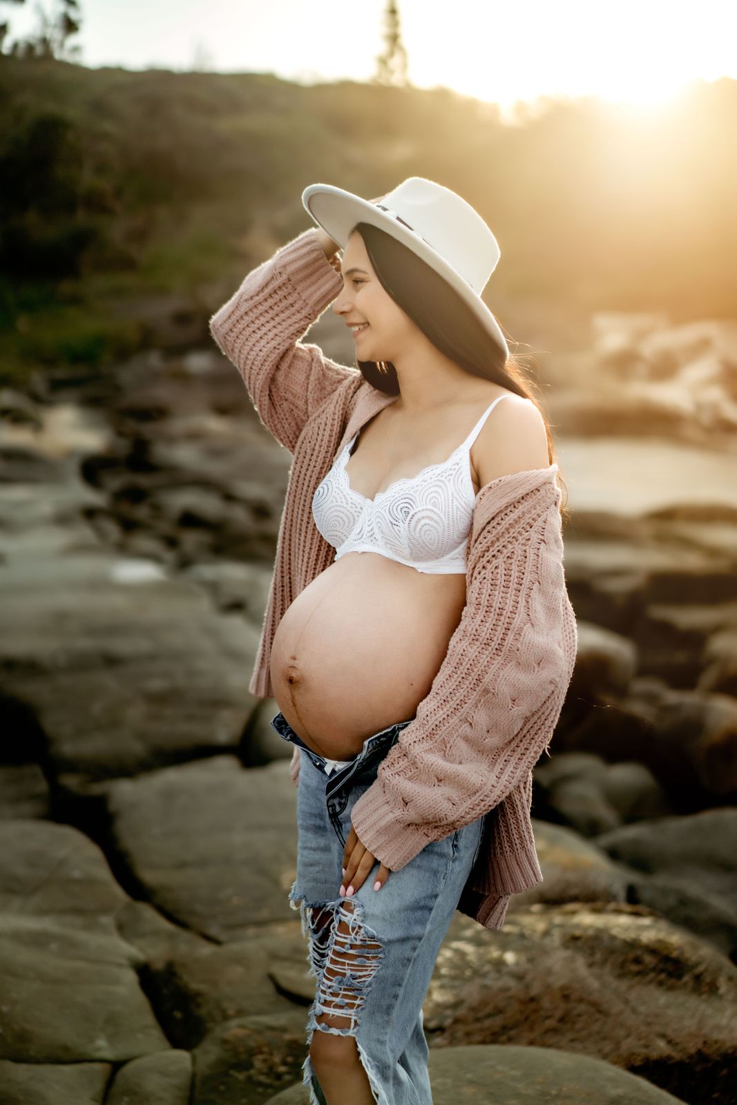 Mum-to-be in a hat and open shirt, backlit on the rocks