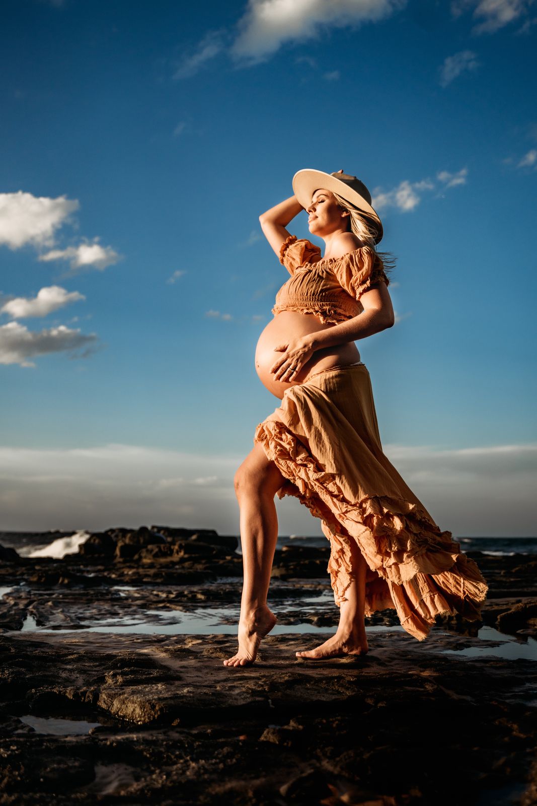 Mum-to-be in a rust dress on the rocks against a blue sky