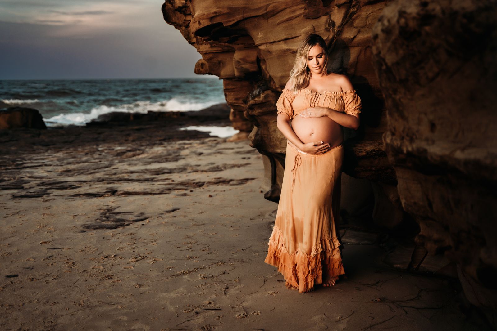 Mum-to-be in a rust dress at the mouth of a sea cave