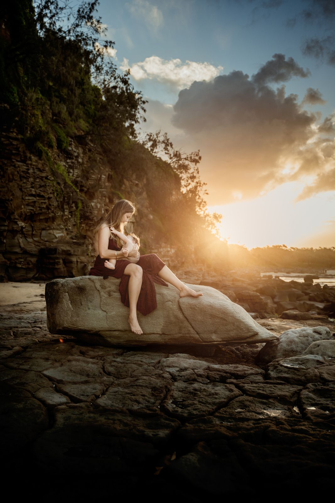 Mum sitting on a sandstone ledge under a dramatic sunset sky